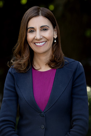 Vision Australia Chief Practitioner Amelia Ukovic is smiling at the camera. She has long brown hair and is wearing a navy suit and fuchsia top