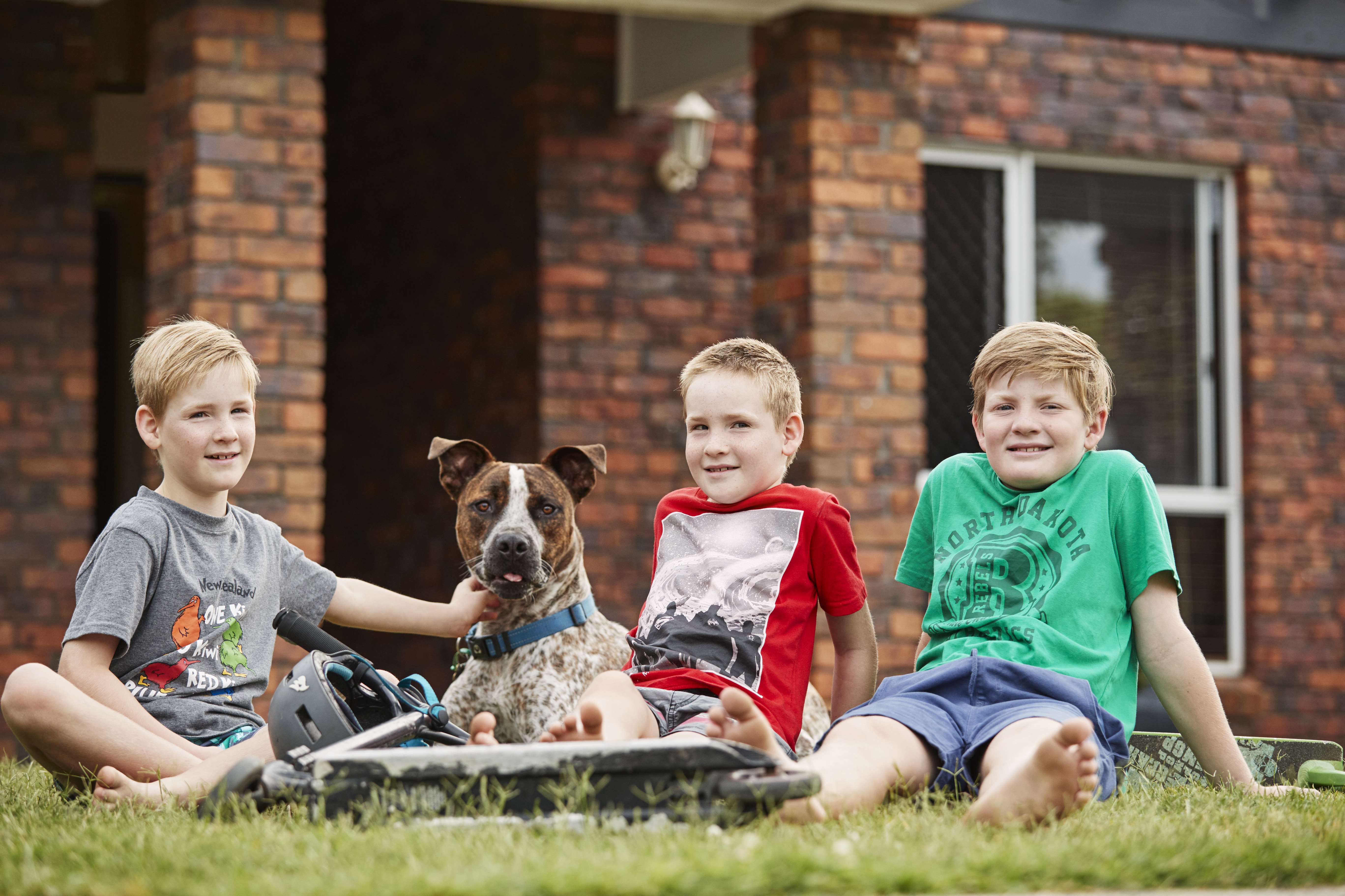 Three children sitting on the grass with their dog out the front of their home