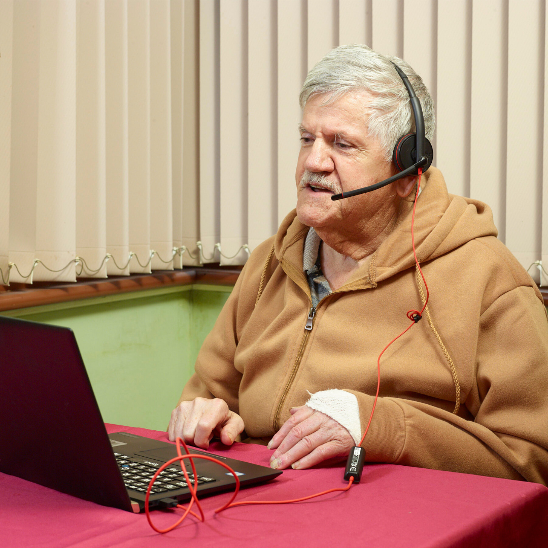 A Vision Australia client sits as his dining table, wearing a headset as he is in his telehealth appointment.