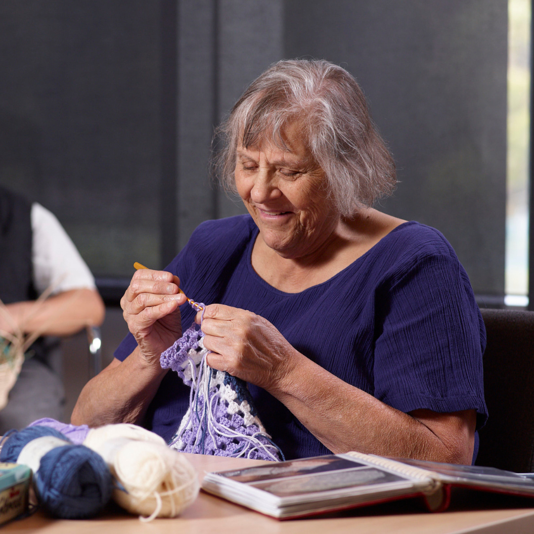 A woman with vision loss smiles as she enjoys knitting.